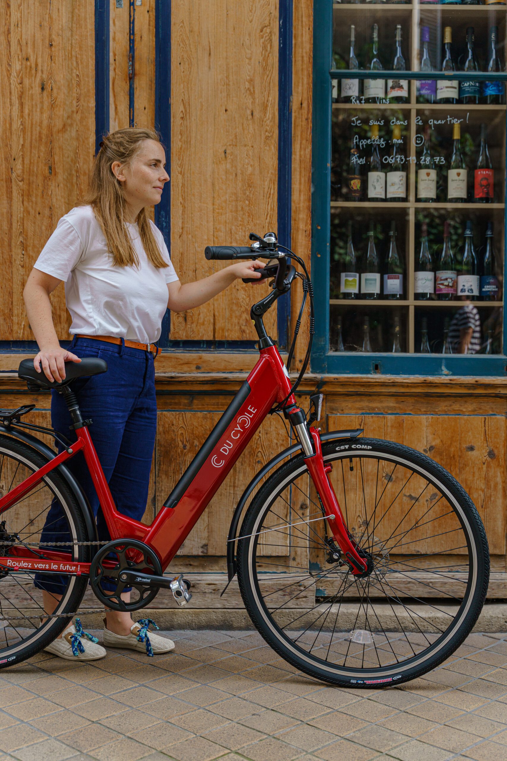Vélo électrique Ariane rouge, vue de droite, entière, avec une personne à côté, arrière plan fond bois