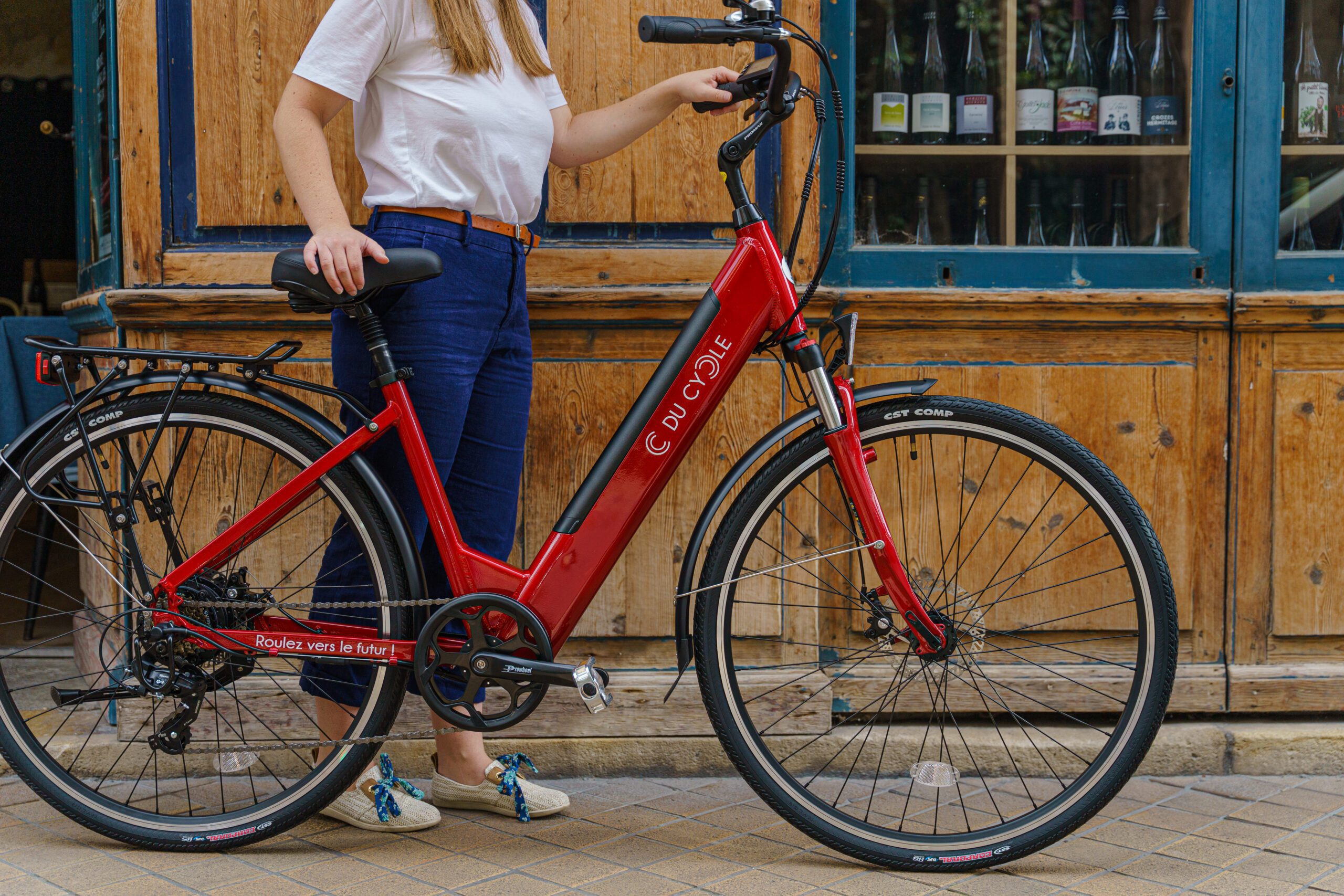 Vélo électrique Ariane rouge, vue de droite, avec une personne à côté, arrière plan fond bois