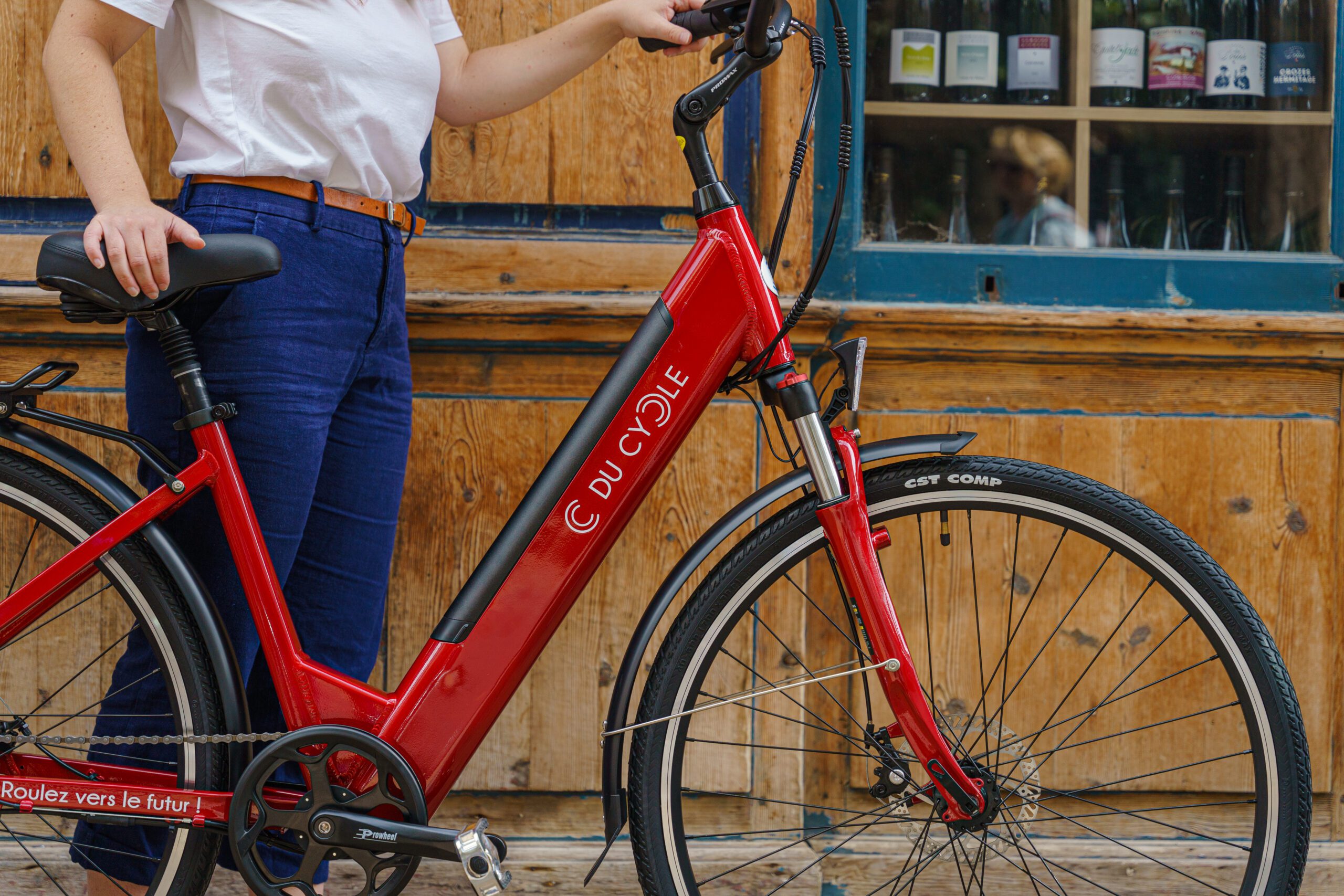 Vélo électrique Ariane rouge, vue de droite, zoome avec une personne à côté, arrière plan fond bois
